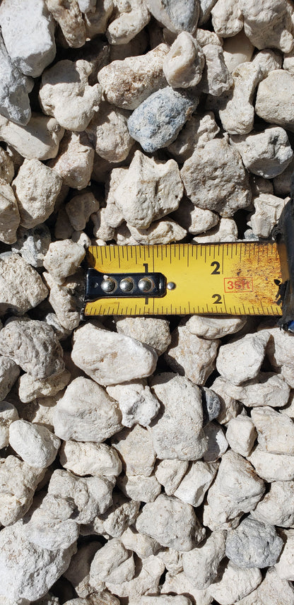 Close-up of #57 Limestone gravel with tape measure showing stone size, ideal for landscaping, driveways, and construction projects.