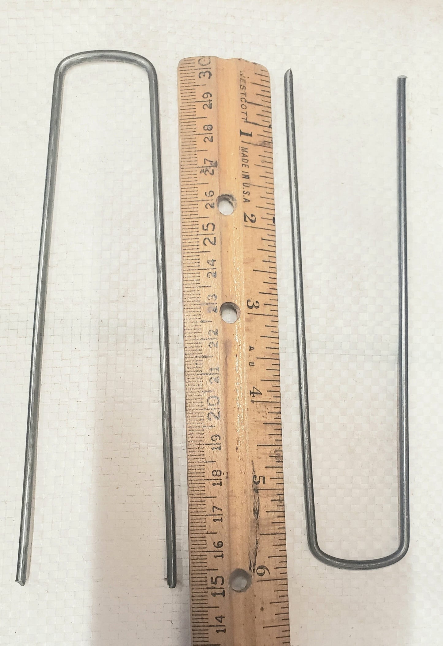 6-inch galvanized landscape staples placed next to a ruler showing exact length for weed barrier, landscape fabric, and garden installation