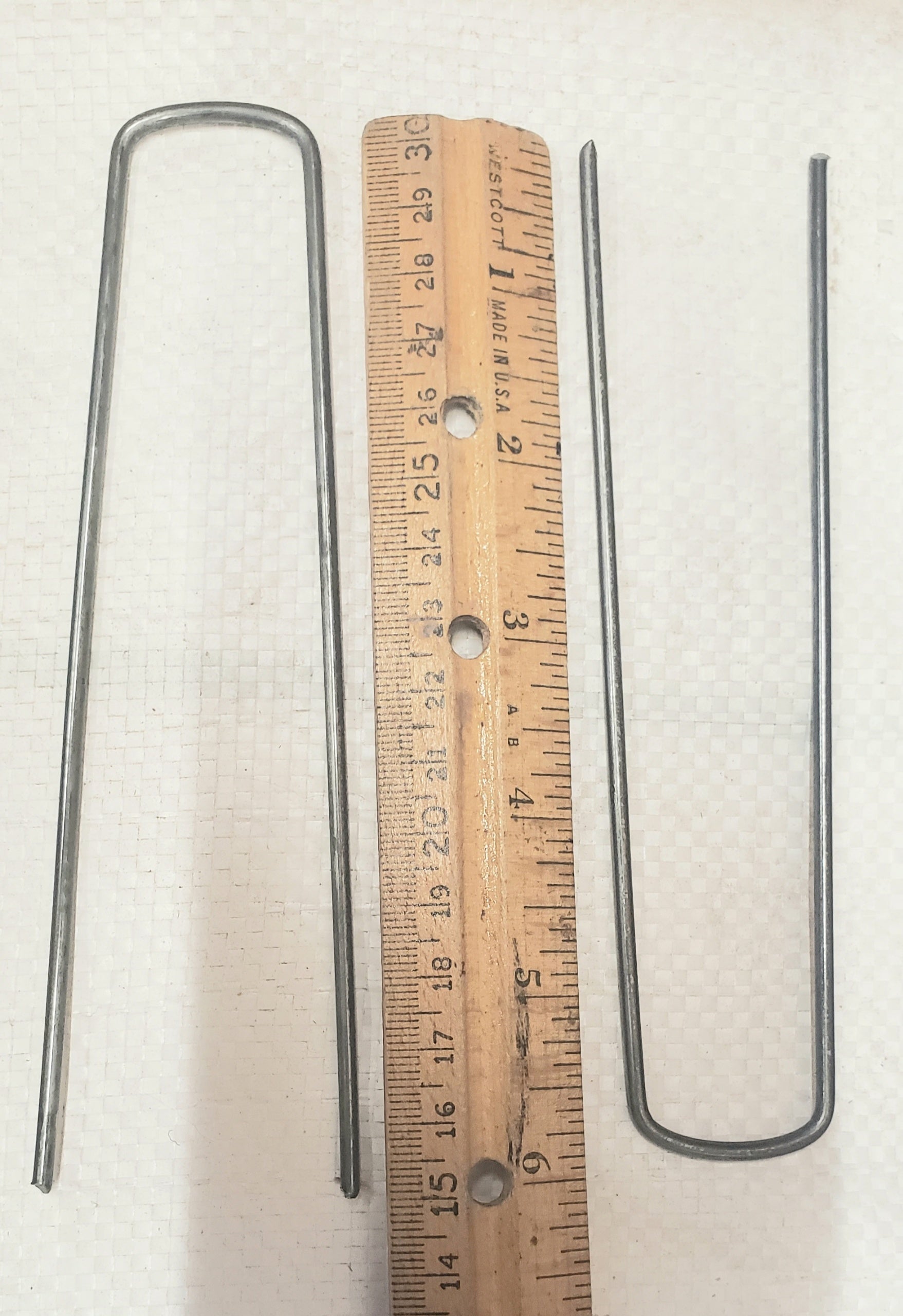 6-inch galvanized landscape staples placed next to a ruler showing exact length for weed barrier, landscape fabric, and garden installation