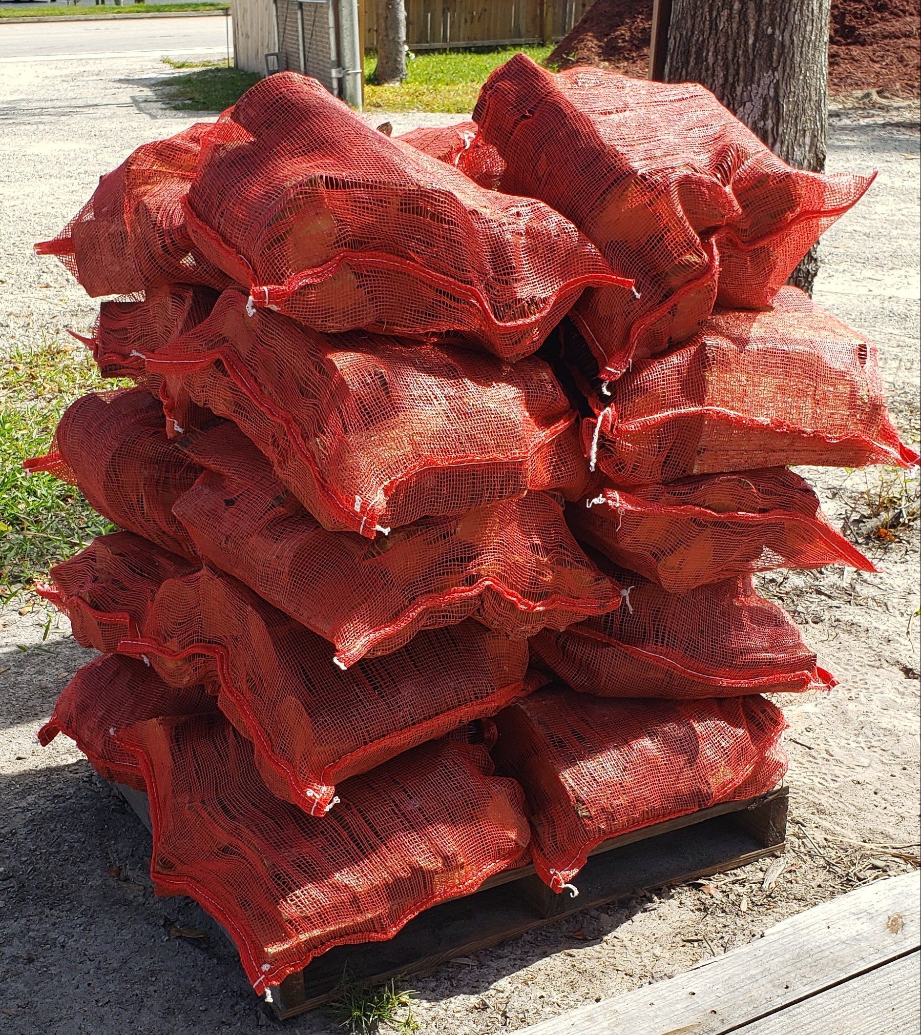 Bags of premium firewood stacked on a pallet, each bag containing 6–8 seasoned logs for easy pickup at Mulch and Stuff