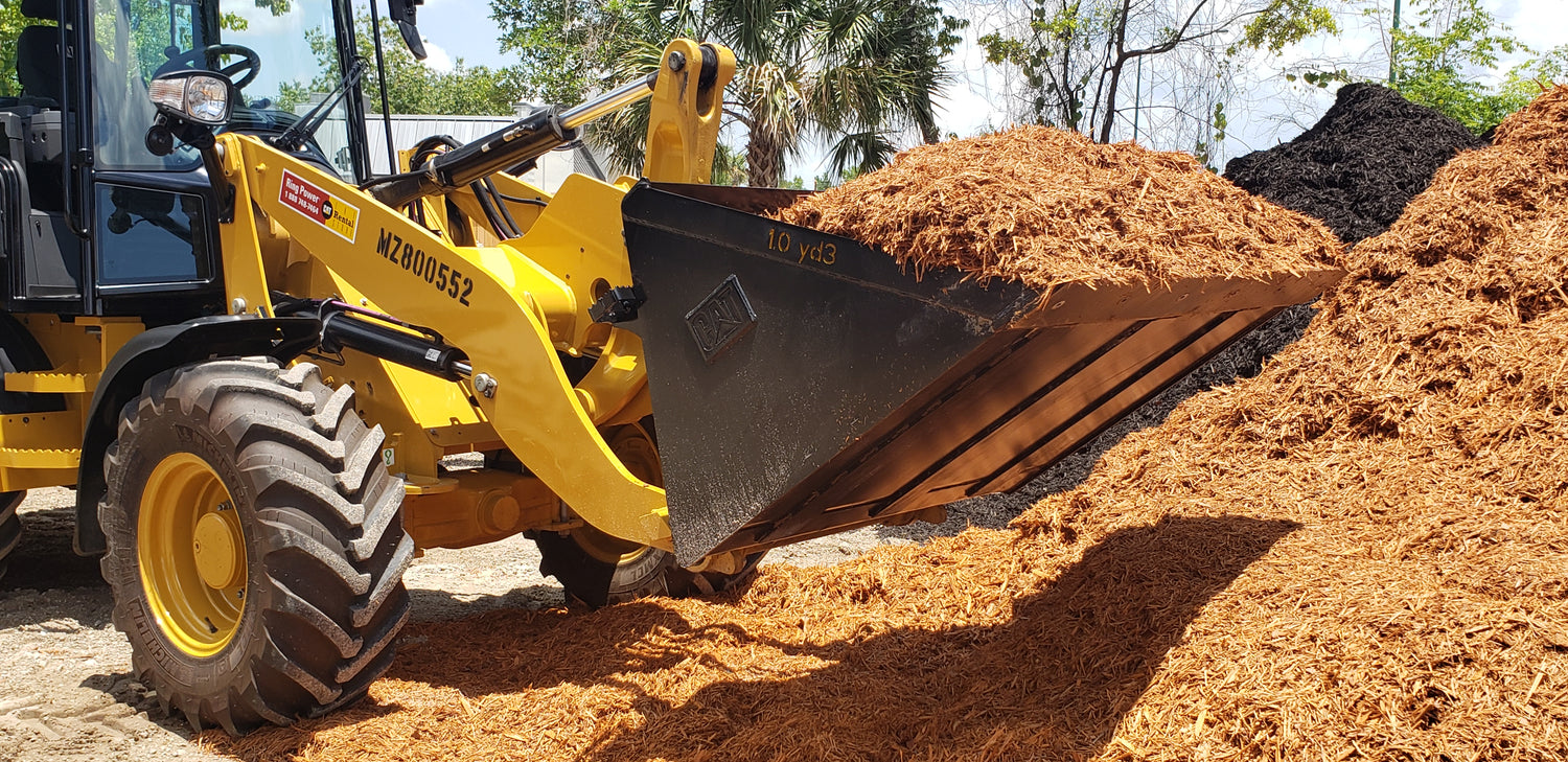 CAT loader in the Mulch and Stuff landscape materials yard in Ormond Beach, showing stocked piles of mulch, rock, sand, and soil ready for full, honest-load deliveries.